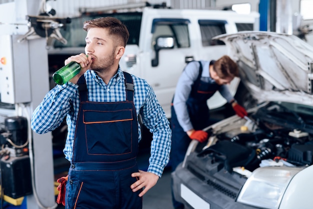 O auto mecânico novo está bebendo uma cerveja na garagem.