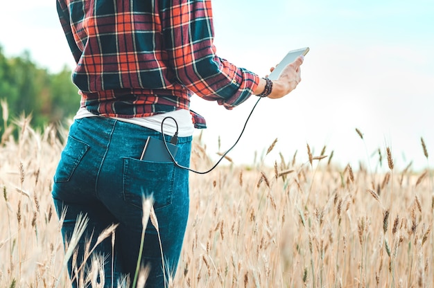 O banco de energia no bolso de trás de uma garota em um campo amarelo carrega o telefone.