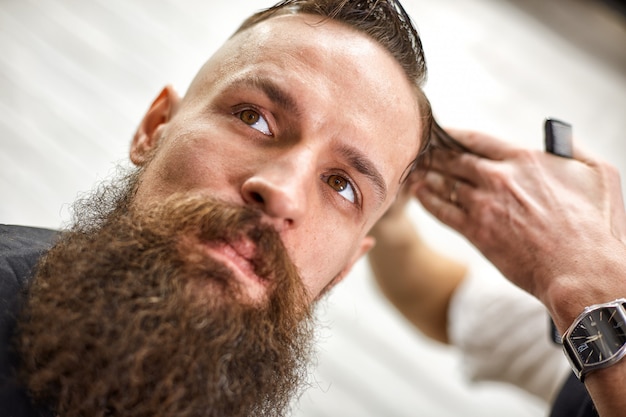 O barbeiro estiloso corta um homem brutal com uma barba espessa.