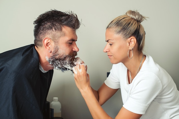 O barbeiro pinta a barba e o bigode na cor preta de um homem moderno na barbearia. Cabeleireiro cabeleireiro lavando a barba do cliente - homem relaxando no salão de beleza de cabeleireiro. Limpeza de barba barbearia.