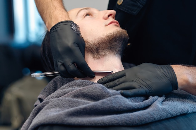 O barbeiro profissional faz a barba do cliente com uma navalha.