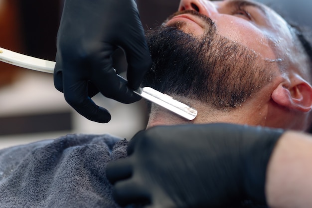 O barbeiro profissional faz a barba do cliente com uma navalha.