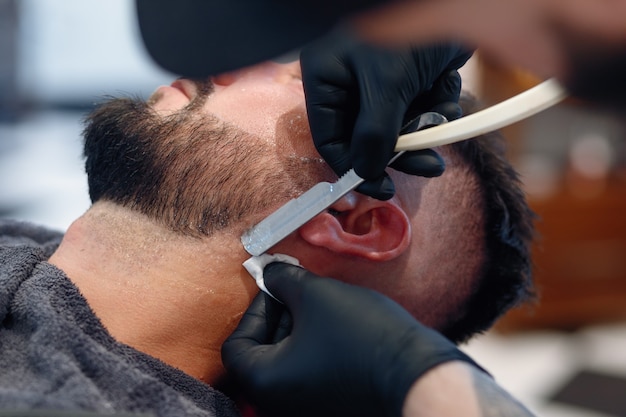 Foto o barbeiro profissional faz a barba do cliente com uma navalha.