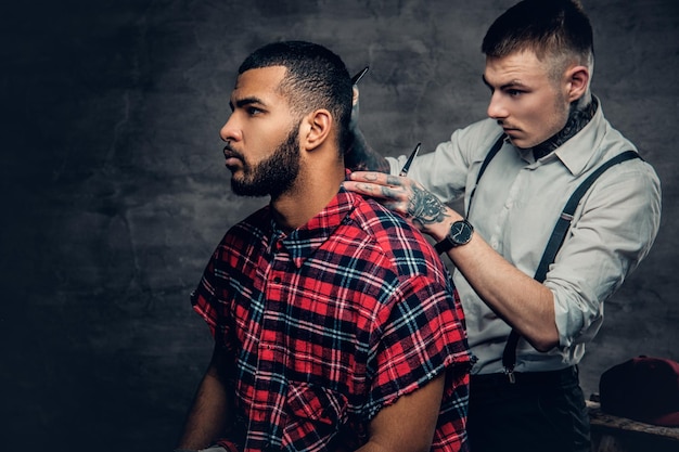 O barbeiro tatuado corta a barba de um homem barbudo preto.