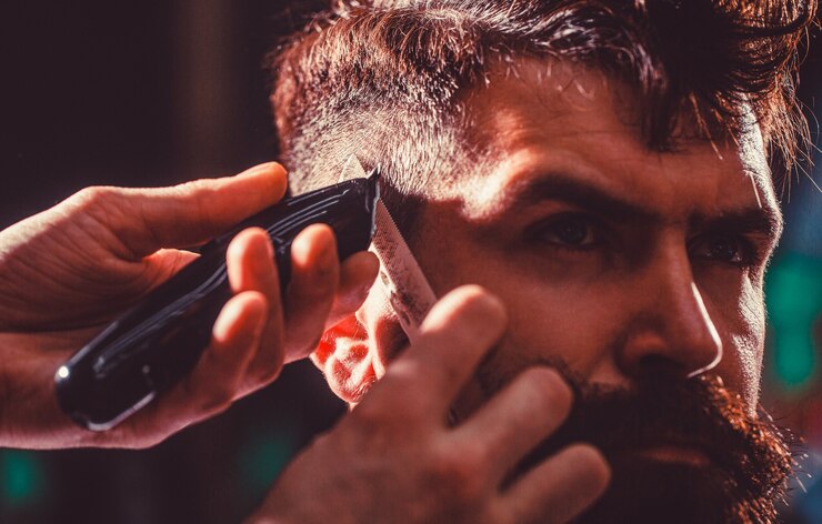 Foto o barbeiro trabalha com o aparador de cabelo. cliente hipster cortando cabelo. mãos do barbeiro com a máquina de cortar cabelo, close-up. homem barbudo na barbearia. conceito de corte de cabelo. homem visitando cabeleireiro na barbearia.