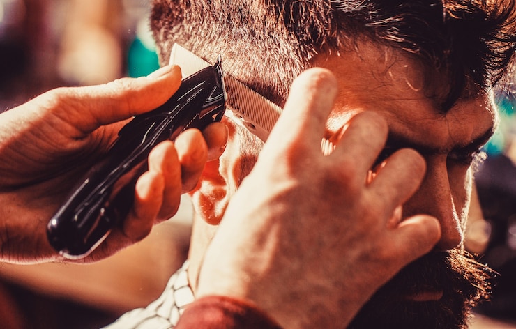 Foto o barbeiro trabalha com o aparador de cabelo. cliente hipster cortando cabelo. mãos do barbeiro com a máquina de cortar cabelo, close-up.