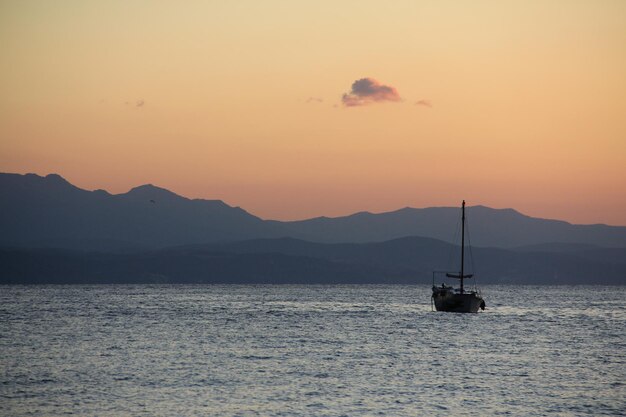 O barco navega à beira-mar ao nascer do sol, no contexto da montanha.