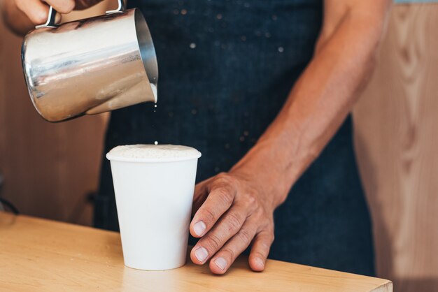 O barista derrama o leite de uma lata no café em um copo descartável de papel