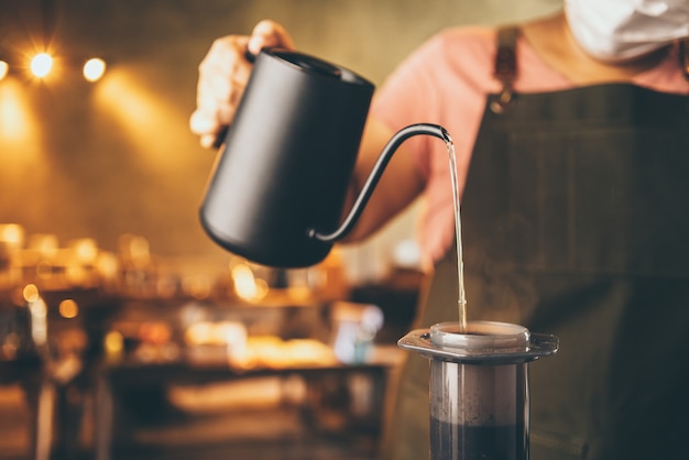 O barista profissional faz uma bebida fresca com chá e leite na xícara, bebida saborosa no bar café, mão segurando leite com leite em uma cafeteria ou restaurante de comida, barman trabalhando em uniforme de cafeteria