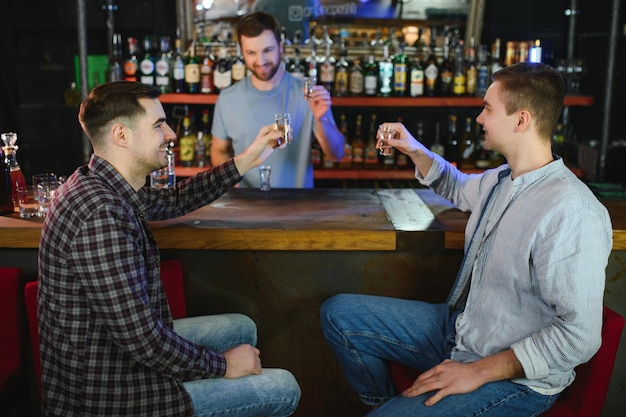 O barman atraente está sorrindo e recebendo pedidos de dois homens sentados no balcão do bar no pub