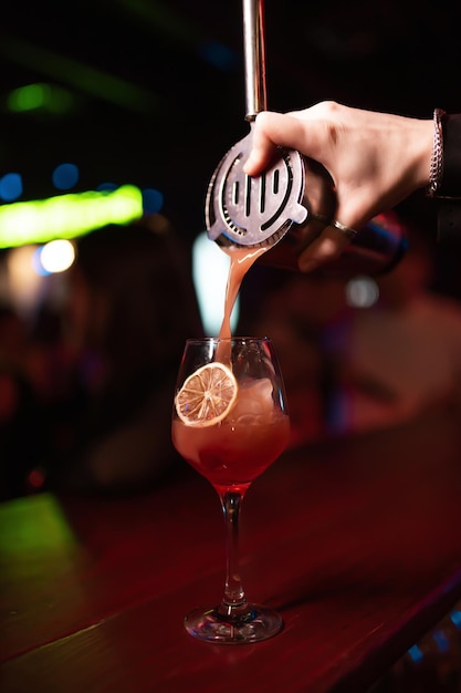 O barman despeja o coquetel acabado da coqueteleira em um belo copo de coquetel no bar álcool na mesa do bar