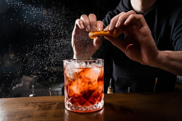 O barman espreme a casca de laranja e espalha o suco sobre o Negroni no copo O barman prepara o clássico coquetel Negroni no bar