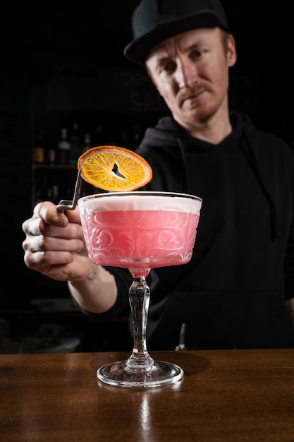 O barman está decorando o coquetel alcoólico do clube Clover rosa com uma fatia de laranja no bar O barman mistura vermute seco de limão e gin para preparar o coquetel Clover club