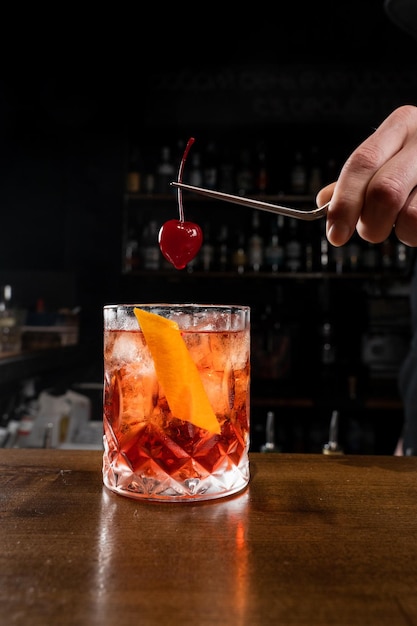 O barman está segurando a cereja sobre o coquetel Negroni no copo O barman prepara o clássico coquetel Negroni no bar