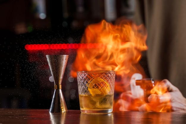 O barman faz fogo sobre um coquetel com casca de laranja de perto.