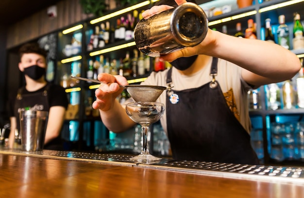 O barman preparou-se para despejar um coquetel em um copo refrigerado através de um coador Foto horizontal