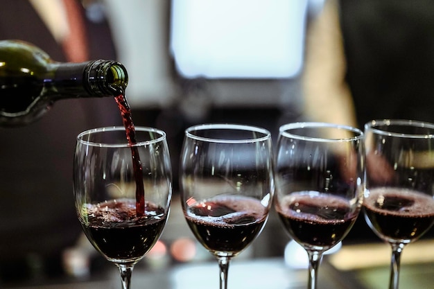 O barman serve vinho tinto em taças no bar. Sommelier masculino servindo vinho tinto em taças de vinho de cabo longo.