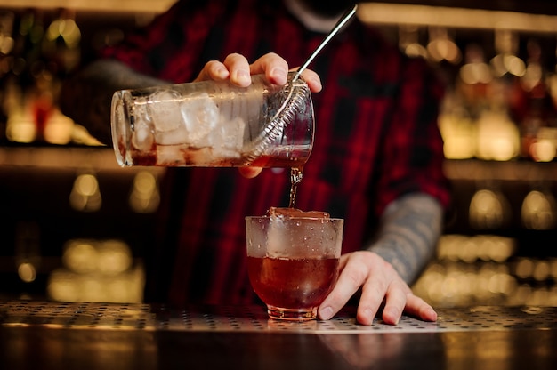O barman servindo um coquetel de uísque forte e fresco em um copo com um grande cubo de gelo