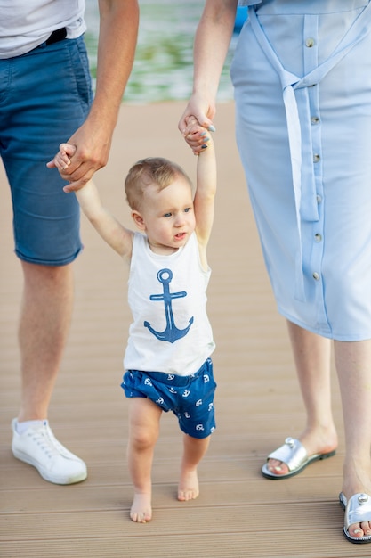O bebê aprende a andar dando os primeiros passos para segurar as mãos dos pais, mães e pais no verão descalço