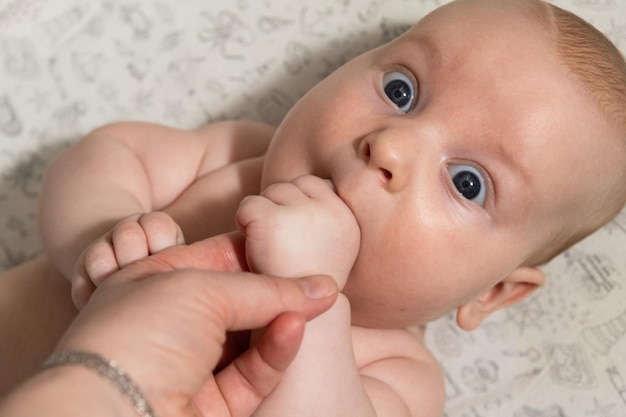 O bebê brinca e come as mãos e olha para a câmera