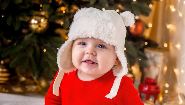 O bebê de Natal está sorrindo. Uma menina bonitinha em um vestido vermelho e um chapéu branco expressa emoções.