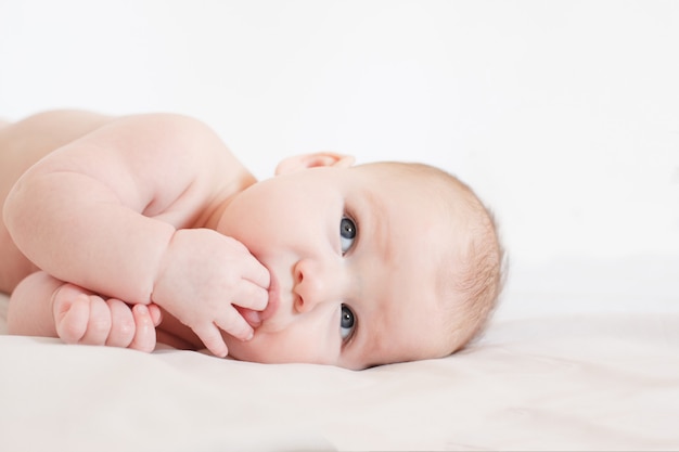 Foto o bebê encontra-se em uma cama em um fundo branco com a mão na boca