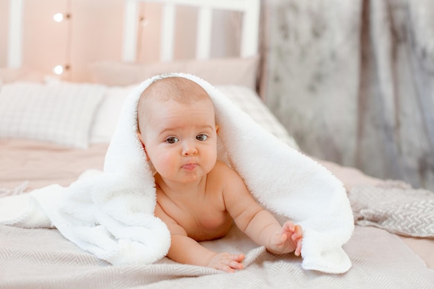 O bebê está deitado coberto com uma toalha na cama em casa após o banho