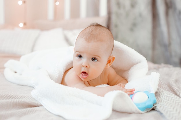 O bebê está deitado coberto com uma toalha na cama em casa após o banho