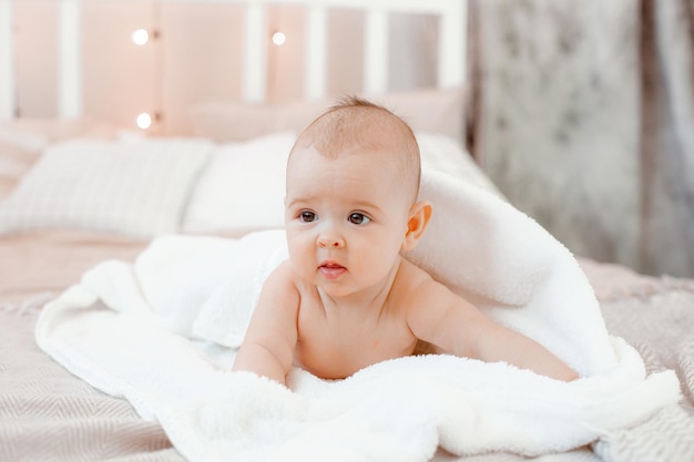O bebê está deitado coberto com uma toalha na cama em casa após o banho