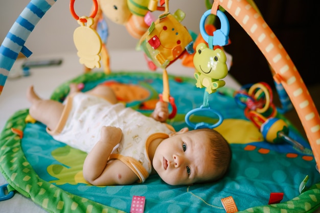 O bebê está deitado em uma esteira de jogos e segura um chocalho na mão