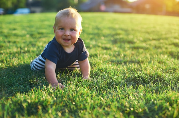 O bebê está rastejando em um gramado verde na luz solar da manhã.