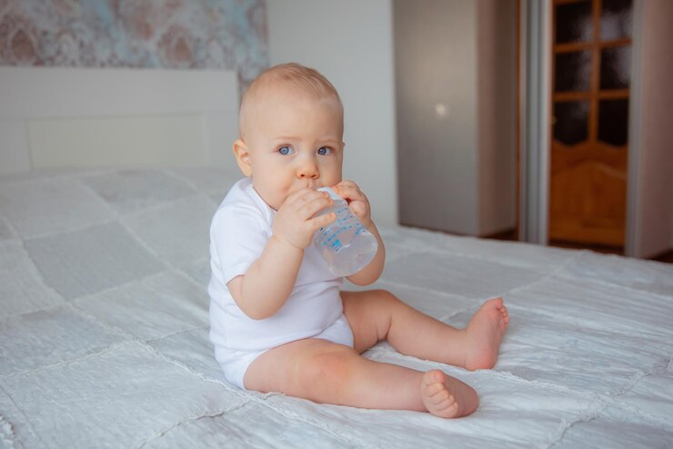 Foto o bebê está sentado na cama bebendo água de uma garrafa