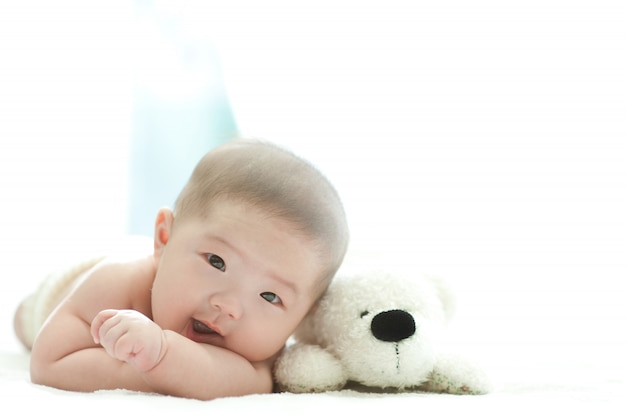 O bebê está sorrindo na frente em uma cama branca com fundo branco.