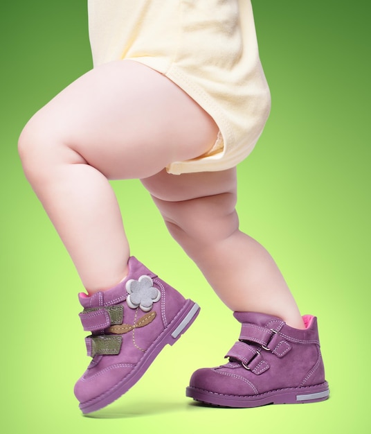 O bebê estiloso vai de botas. em um fundo verde