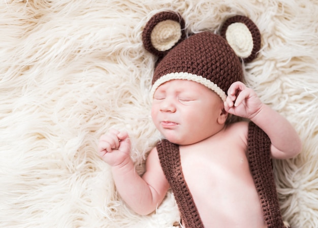 O bebê feliz pequeno bonito encontra-se em uma fantasia de urso em um branco. recém-nascido em um chapéu com orelhas em um branco