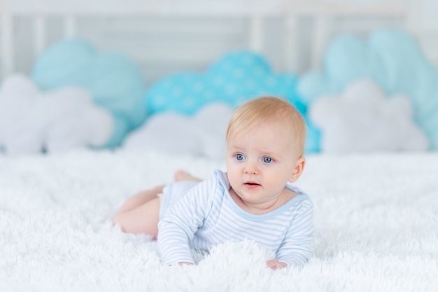 O bebê na cama de pijama azul vai para a cama ou acorda de manhã, bebê menino loiro de seis meses