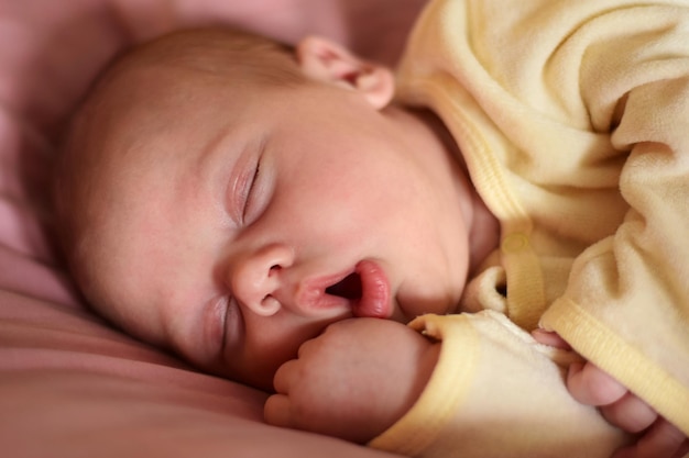 O bebê recém-nascido dorme com a boca aberta. uma, duas semanas de idade. menina infantil dormindo ou acordando deitada na cama roxa em casa. nova vida e conceito de crescimento. pessoas reais. infante de pijama amarelo.