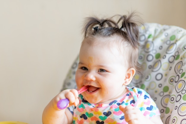 O bebê se come com uma colher de purê de batata de um pote, o conceito de comida para bebê
