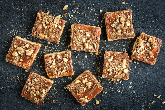 O biscoito amanteigado caseiro do caramelo esquadra biscoitos com as porcas colocadas na forma de um quadrado no fundo preto com migalhas.