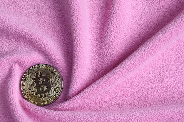 O bitcoin dourado encontra-se em um cobertor feito de tecido de lã rosa claro macio e fofo