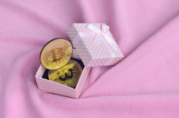 O bitcoin dourado encontra-se em uma pequena caixa de presente rosa com um pequeno laço em um cobertor