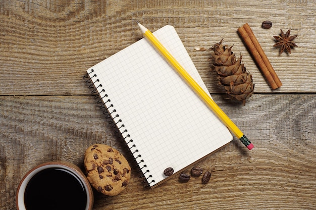 O bloco de notas aberto e a xícara de café com biscoitos de chocolate na velha mesa de madeira. Vista do topo