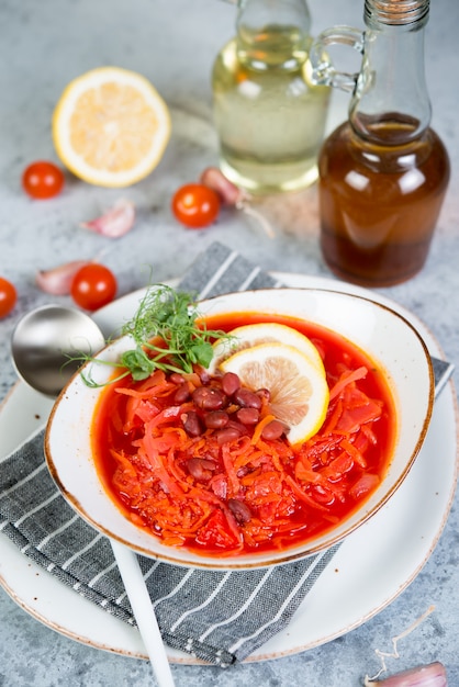 O borscht ucraniano do vegetariano com feijões vermelhos em uma placa branca está em um fundo cinzento do concreto.