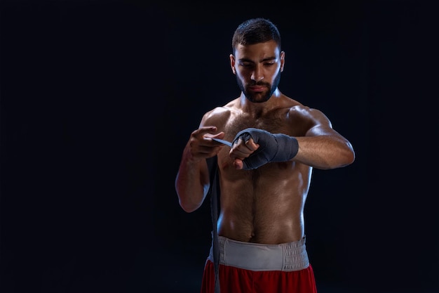 O boxeador esportivo puxa os envoltórios de pulso da mão. Modelo masculino oriental isolado no fundo preto.