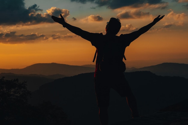 Foto o braço bem-sucedido das conquistas da silhueta está no topo da colina comemorando o sucesso com o pôr do sol