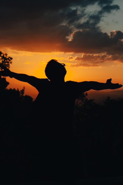 Foto o braço bem-sucedido das conquistas da silhueta está no topo da colina comemorando o sucesso com o pôr do sol