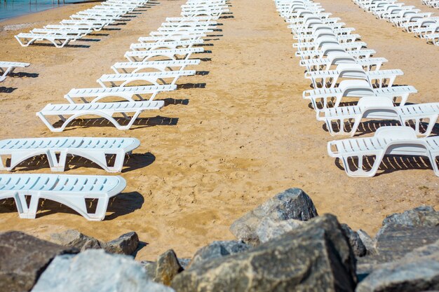 O branco sunbed na praia da areia no mar, conceito do resto do mar do verão.