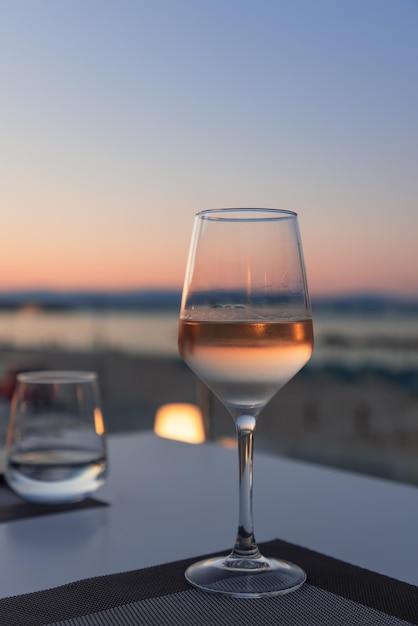 O brilho rosa do pôr do sol junto com o mar e a praia de areia em um copo de vinho branco concentrado no café da praia