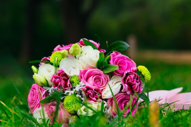 O buquê da noiva Um buquê de flores brancas vermelhas e rosa com vegetação com uma fita encontra-se em um gramado verde