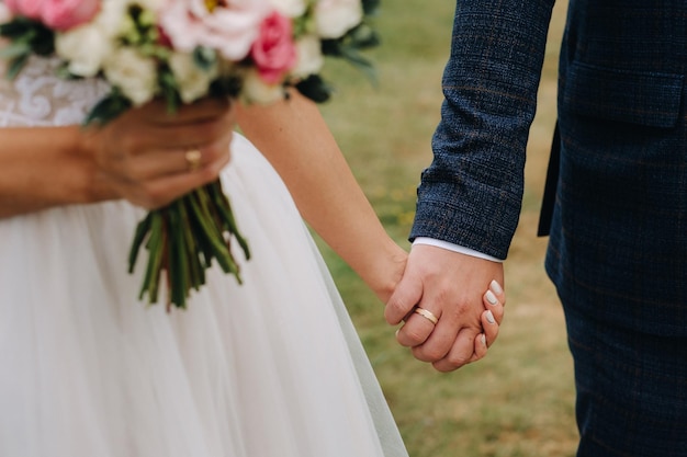 O buquê de casamento da noiva com flores rosa frescas na mão e de mãos dadas com o noivo Detalhes do casamento